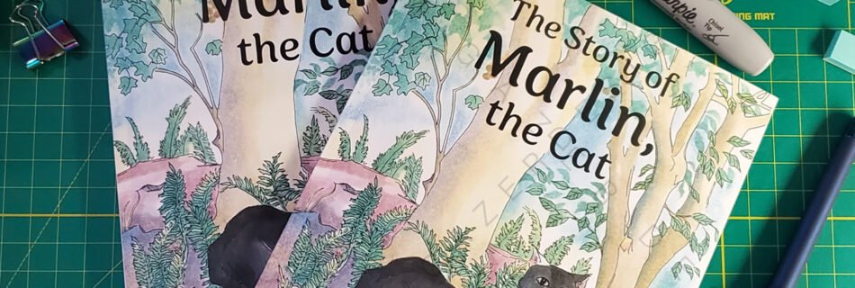 paperback and hardcover copies of the children's book 'The Story of Marlin the Cat' by Ainsley Bloomfield. The cover features a full-color illustration of a black cat in a forest. The image serves as a portfolio piece showcasing professional book layout and print production services, which included preparing the artwork for publication and handling the overall design.